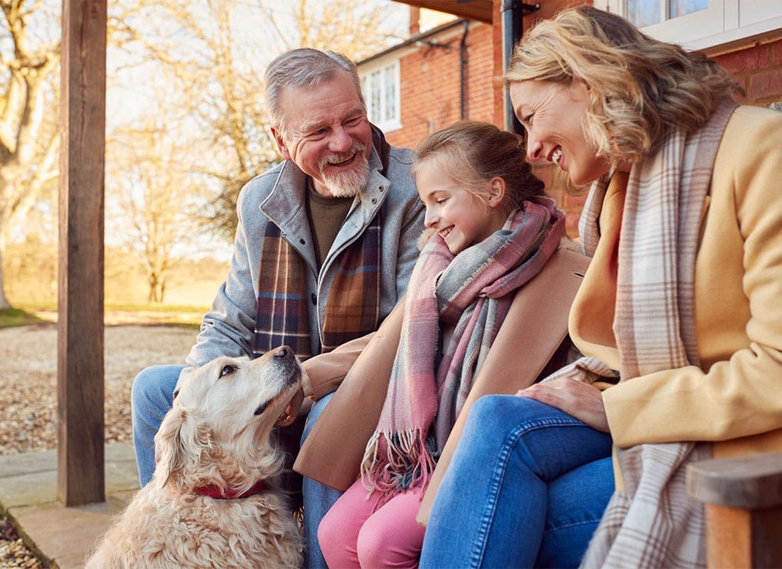 Insurance Solutions - Portrait of a Cheerful Family with a Daughter Sitting on the Back Porch with Their Dog During the Fall